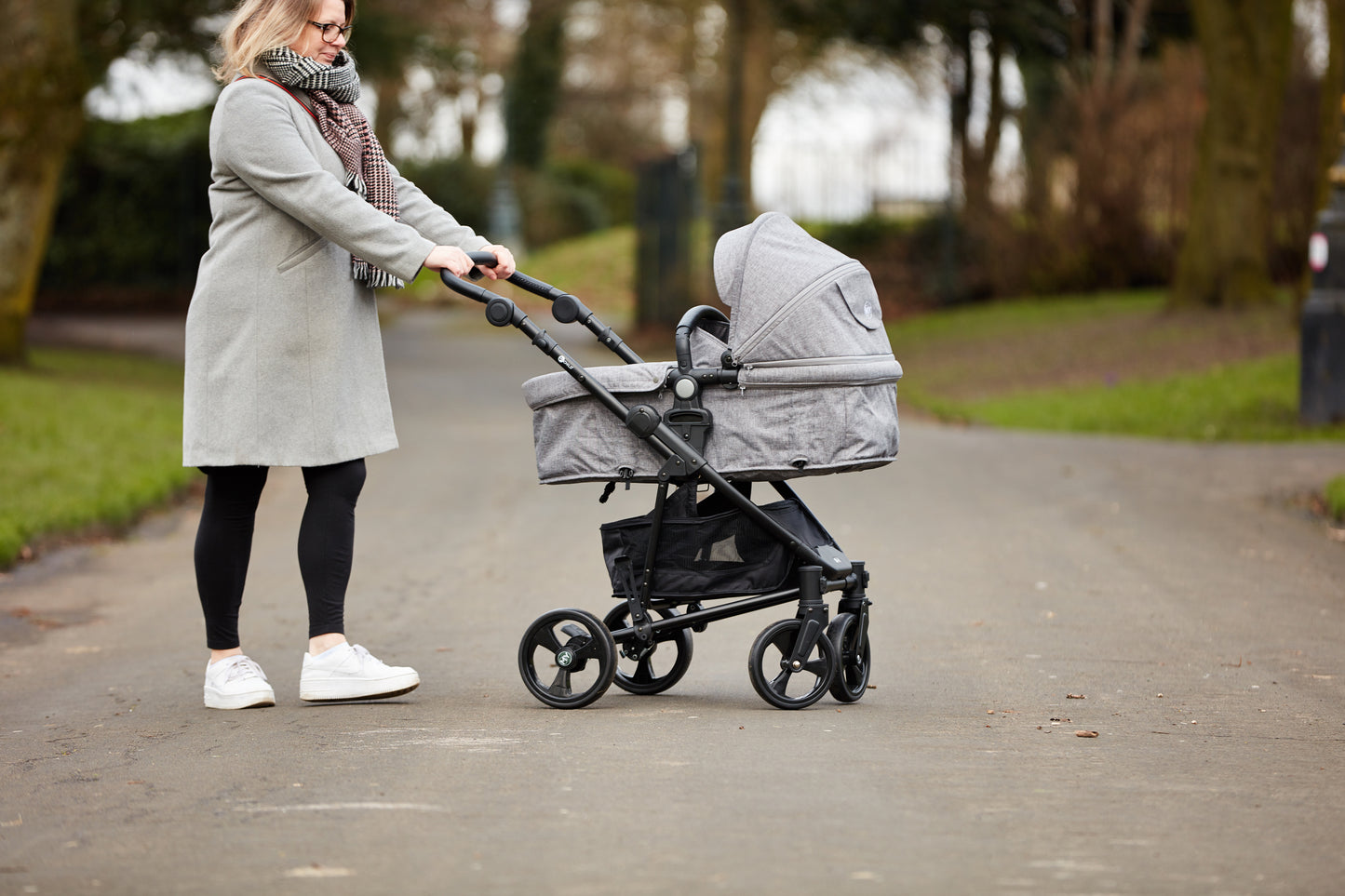 Parent pushing pram with carrycot outdoors, side view