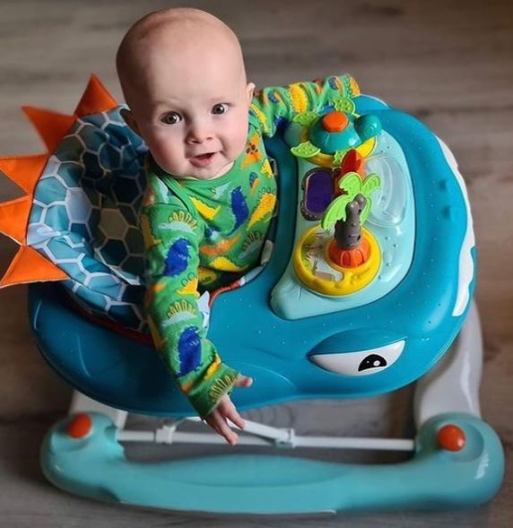 Baby in a colorful dinosaur-themed walker on a wooden floor
