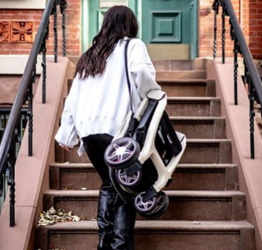 Person carrying a folded stroller up a set of stairs.