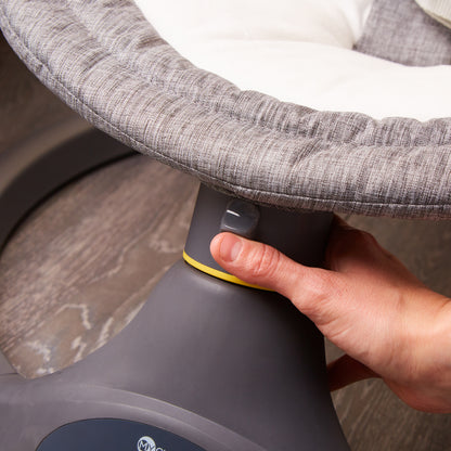 Person adjusting a gray baby bouncer with a hand on a neutral background
