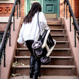 Person carrying folded compact stroller up stairs